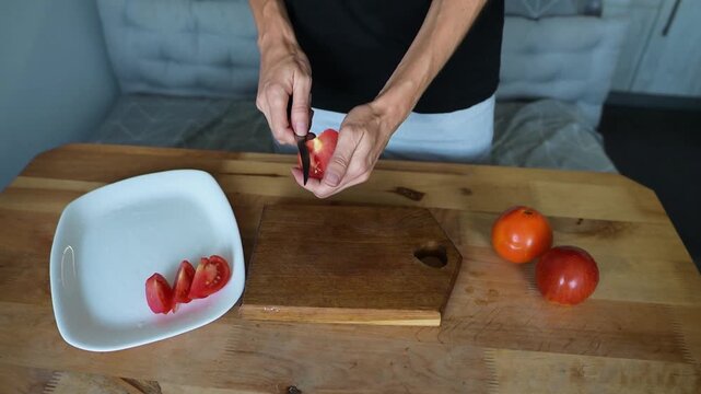 Person slicing fresh red tomato on wooden board and arranging pieces on video Full HD plate