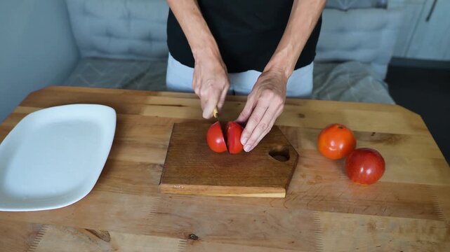 Person slicing fresh red tomato on wooden board and arranging pieces on plate video Full HD