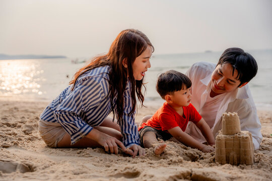 Happy Asian family plays in the sand on the beach.