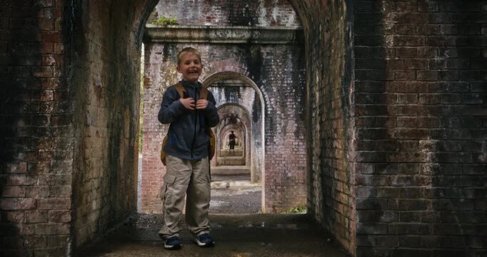 Boy with backpack standing in brick archway under Japanese bridge - steady cam movement in