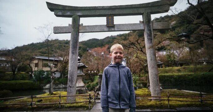 Little boy standing in front of ancient stone torii gate in Japanese village - low, slow motion shot