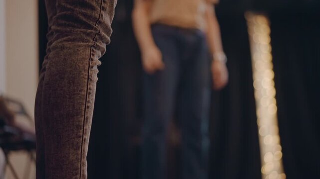 Closeup socked feet on stage floor, nervous performer grounding before audition with blurred instructor in background, soft string lights and dim studio mood, focus on balance posture and subtle