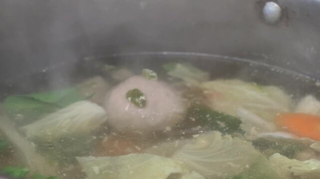 Preparing a delicious and healthy homemade meatball vegetable soup in a boiling pot with hot steam rising up, showcasing culinary lifestyle.
