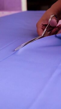 Tailor cutting blue fabric with sharp scissors a close up view of a person using metal to precisely cut piece of smooth along chalk sewing textile clothe fashion craft
