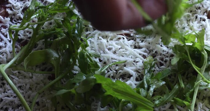 Arugula leaves sprinkled over beef covered with grated hard cheese, carpaccio preparing, close up