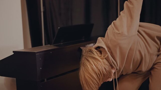 White pianist practicing at piano in dim studio, leaning on instrument under string lights music teacher composing melody, arranging chords, coaching technique and focus during private session
