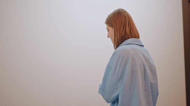 Young white performer in narrow hallway pausing near closed door, visible tension and breath control before entering rehearsal room, blue shirt and introspective posture, subtle interaction