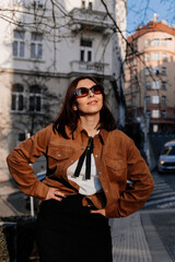 Fototapeta premium Beautiful young woman enjoying a sunset in Prague city. Stylish girl in a fashionable outfit posing outdoors near historic architecture in warm golden light. Urban fashion and lifestyle concept.