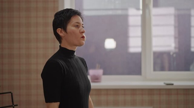 Short hair woman practicing breath control, steady posture and controlled inhale exhale, focus on diaphragm, soft window light, quiet interior classroom mood, vocal training routine