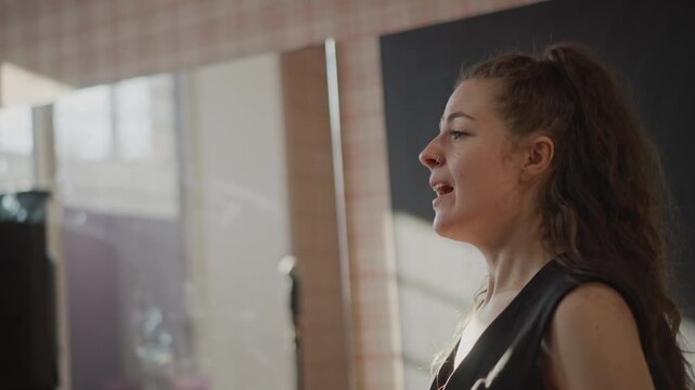 Young white woman directing vocal exercise, energetic masterclass vibe as singer points and guides students, authoritative gestures and timing drills in studio classroom, confident leadership