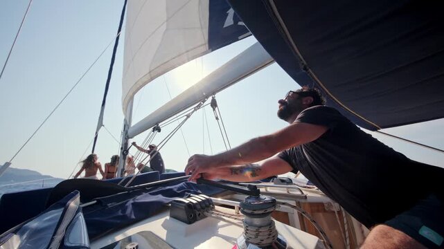 Man operating a winch and handling ropes on a sailing yacht during a sunny sea journey. Sailing lifestyle, nautical activity, yacht operation and summer boating adventure.