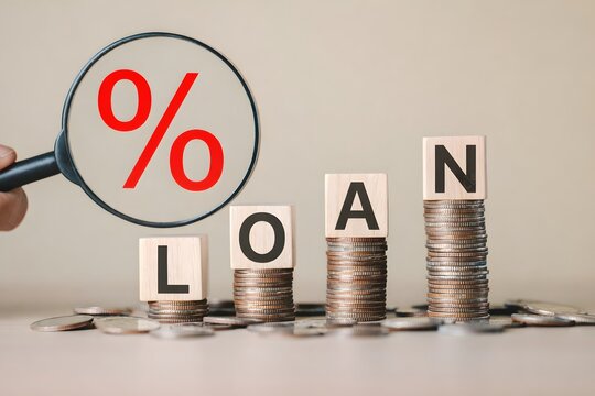 Stacked coins with wooden blocks spelling "LOAN" and a magnifying glass showing a red percentage symbol, representing interest rates, personal finance, debt and loan application process. lending money