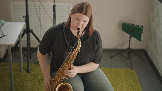 White performer practicing emotive saxophone improvisation in quiet school studio, coach observing off camera, green acoustic panels and keyboard in background, focused expressive mood