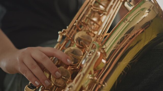 Closeup of saxophone playing. Studio shot of saxophone players demonstrating finger techniques. Focused hands pressing saxophone keys with warm brass reflection in music classroom atmosphere