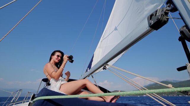 Young woman using a digital camera while sitting on a sailing yacht at sea. Summer vacation, travel content, boating lifestyle, blue water and relaxed nautical leisure.