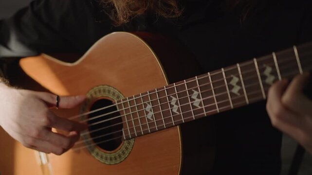 Closeup acoustic guitar hand plucking nylon strings in lowkey studio, focused fingerpicking exercise by male guitarist, warm wood tones and soft shadows conveying concentration and craft.