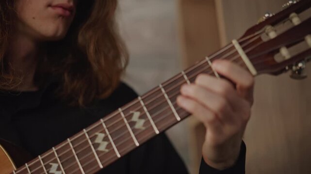 Closeup classical guitar hands playing in studio lesson wooden nylonstring guitar rosette and fretboard visible, longhaired musician demonstrating fingerstyle technique, slow precise plucks, warm