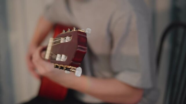Closeup hand tuning guitar headstock, student adjusts machine heads and checks pitch, careful setup and preparation before class, precise motion under teacher supervision in music school environment