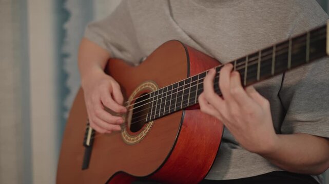 Young musician practicing guitar closeup, student practices chord patterns on nylon string acoustic instrument, fingers moving along frets, gentle strum and focused posture, quiet home lesson