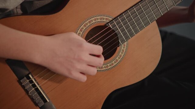 Closeup fingerpicking at soundhole, aspiring performer practices classical arpeggios with fingertip precision, subtle nail technique and warm resonance, rehearsal for recital in private conservatory