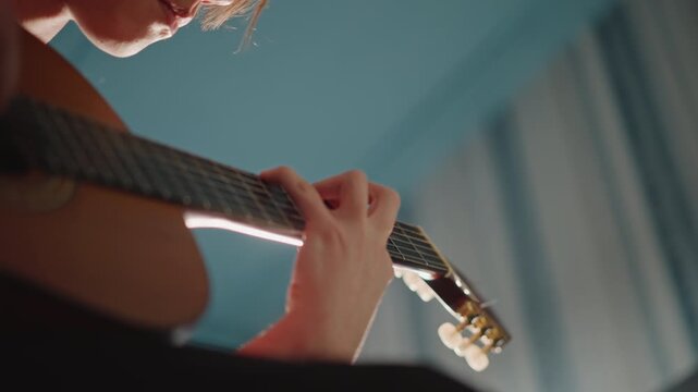 Guitar practice scene. Student rehearses intricate guitar passage. Focused player practicing challenging guitar segment indoors. Student rehearses detailed acoustic guitar piece in dimly lit room