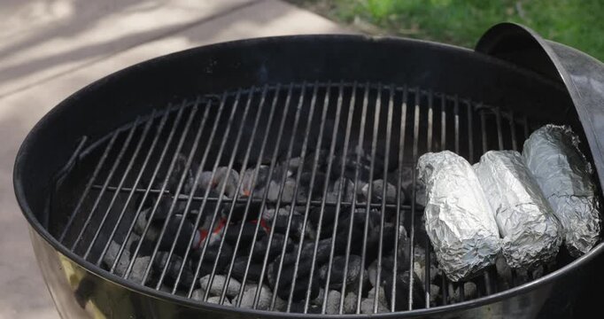 Corn on the cob wrapped in aluminum foil roasting on BBQ