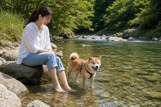 渓流で柴犬と水辺に座る女性