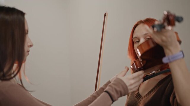 Female violin lesson in small studio, tutor adjusts instrument and bow while student watches warm lighting, closeup hands, supportive coaching, posture correction, stepbystep technique and calm