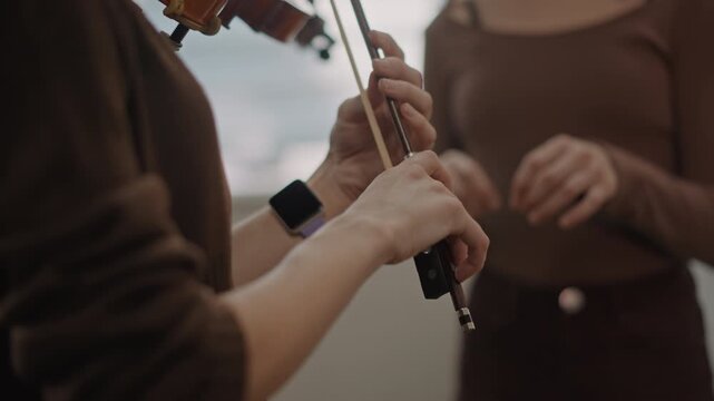 Hands tuning violin during lesson, mentor adjusting pegs while student listens for pitch, closeup of string and pegwork in calm practice room, focused ear training and precise intonation