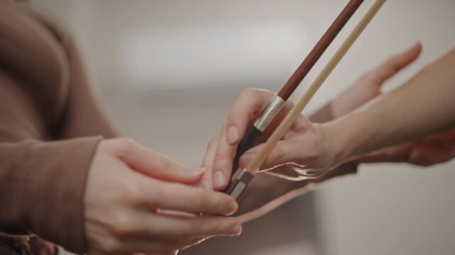 Closeup bow handover white coach demonstrates controlled transfer of bow between teacher and pupil, precise fingertip placement, studio atmosphere and concentrated tutorial moment
