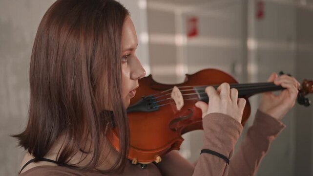 Youth plays violin. Young girl prepares instrument attentively. Teenage girl finetunes violin before practicing carefully. Female teenager adjusts her violin in quiet preparation for lesson