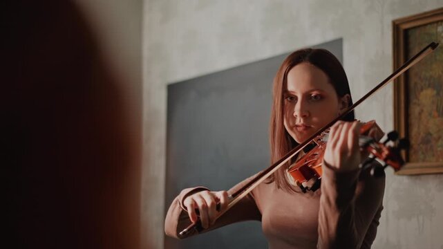 White woman practicing violin closeup, cozy classroom setting with painting and soft window light, student receiving technique tips, focused bowing and phrasing, warm tones and calm expression
