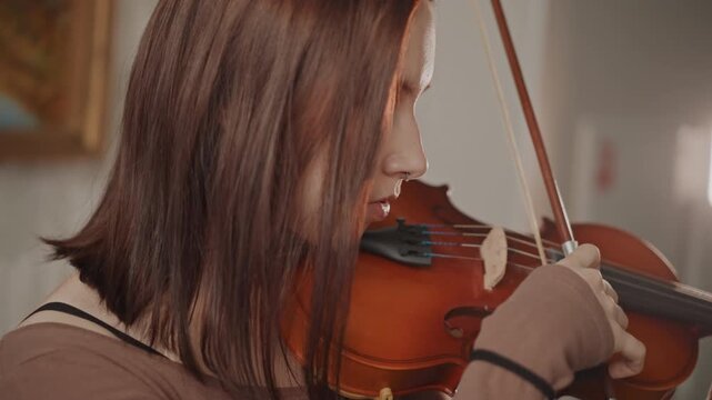 Focused musician practicing in studio. Studio scene showing concentrated violinist during practice session. Side view of dedicated violinist in studio focusing on their performance preparation