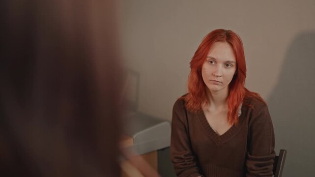 Redhaired white student sits by keyboard, listening as instructor demonstrates bow technique in intimate practice room, anxious expression, warm vintage lighting, candid portrait.