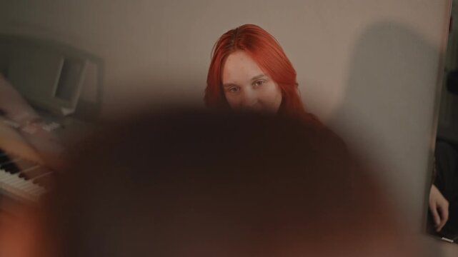 Candidate shows confident composure. Tressed performer awaits assessment with poise and grace. Redhaired artist stands composed as mentor provides gentle feedback during final evaluation