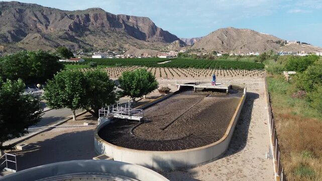 Aerial view of a modern wastewater treatment plant oxidation ditch concrete tank set amidst agricultural fields and arid mountains showcasing sustainable water management environmental industrial ecol