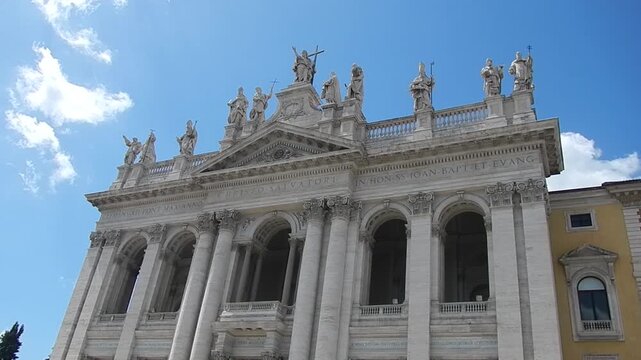 Facade of Basilica of St. John in Lateran in Rome i Italy with statues of Lord Jesus Christ and saints, loggia of blessings and blue sky with slowly moving white clouds. Topics: church, Christianity