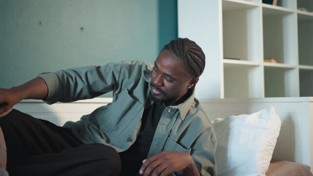 Black man sitting up on bed, preparing to reach for phone and call for help focused expression, steadying with hand on bedside, rising from blanket, home interior, determination to seek medical
