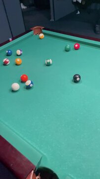 High angle shot of a white cue ball hitting and smashing a racked triangle pyramid of colorful numbered balls on a green felt pool table.