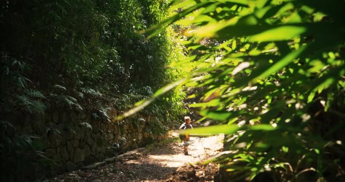 Kid with backpack walking down dirt road in Japanese forest with breeze - handheld shot