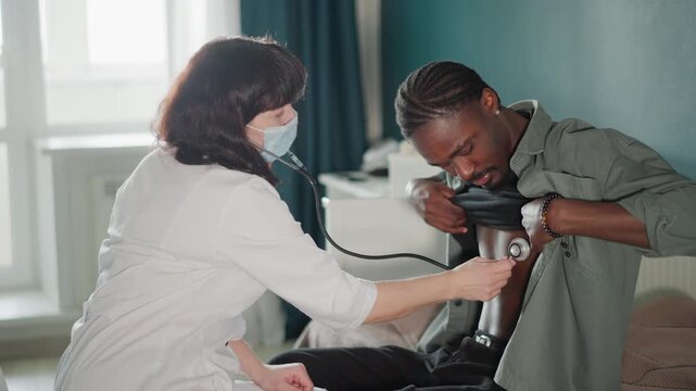 Black male patient home chest exam with white nurse using stethoscope and mask, calm livingroom setting, seated on chair, paramedic bag nearby, reassuring touch during vitals check, professional