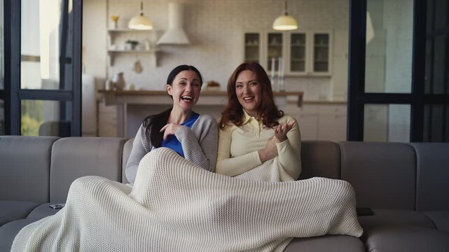 Joyful middle-aged women watching comedy show on TV and laughing at home