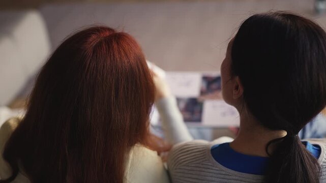 Top view of mother showing family photos to adult daughter, happy memories