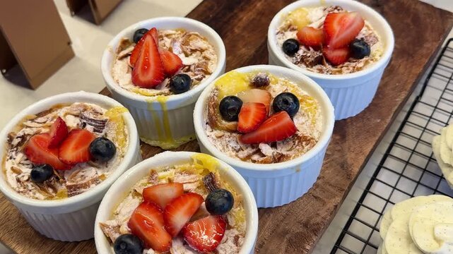 Five white ceramic cups with healthy chia pudding and oatmeal topped with strawberries and blueberries in restaurant display