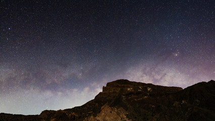 Breathtaking night sky full of stars and the Milky Way galaxy glowing above a dark volcanic mountain ridge silhouette. © Dniel