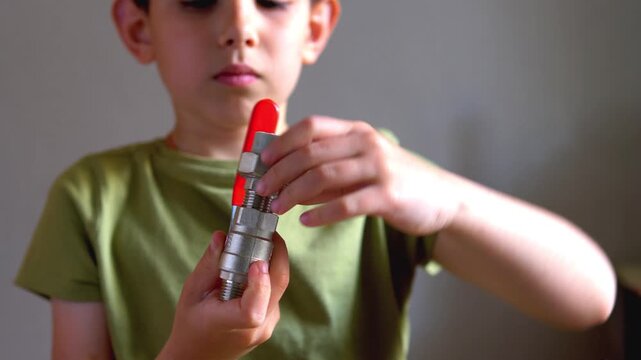 Young boy assembling a metal ball valve with a red handle during a hands-on STEM engineering project; conceptual for childhood curiosity, practical life skills, and DIY education