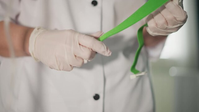 Nurse sets tourniquet. Sterile band placement procedure. Careful positioning and inspection of tourniquet by nurse. Clinic nurse meticulously prepares and verifies green tourniquet carefully