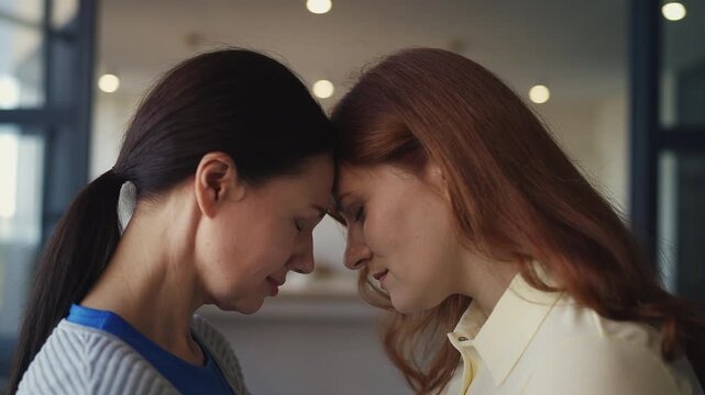 Two sisters in their 40s leaning foreheads while reconciling after argument