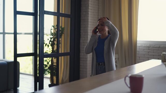 Worried middle-aged woman talking on smartphone at home, stressed by news