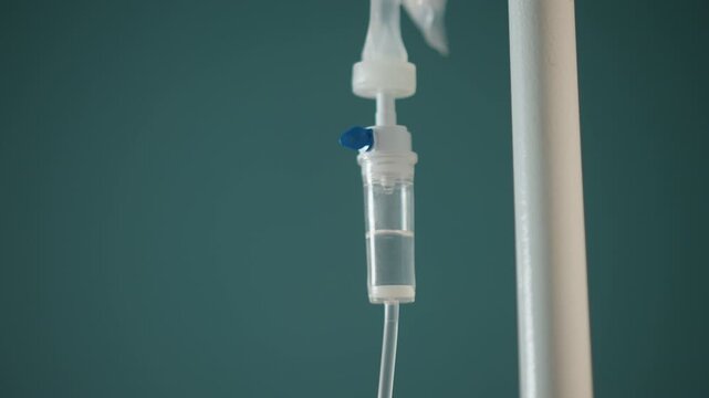Iv drip hanging on teal pole home nurse adjusts infusion during home visit, closeup of drip chamber and tubing, saline droplets visible, clamp and connector in focus, calm clinical atmosphere ideal